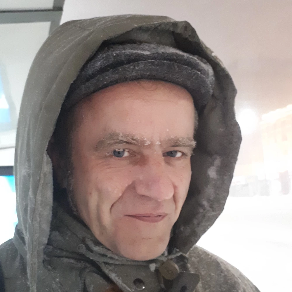 Person mit Kapuze l&auml;chelt in die Kamera, Schneeflocken im Gesicht, unscharfer Hintergrund mit Schneefall.